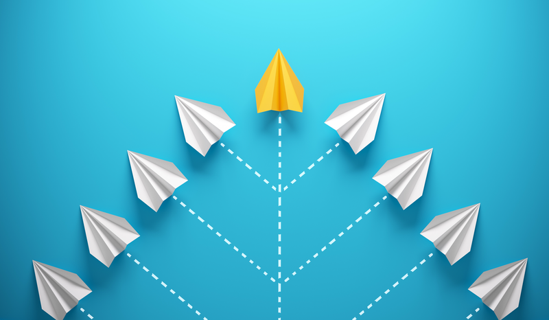 White paper planes diverge from a central point, with one yellow plane leading upward, against a blue background.