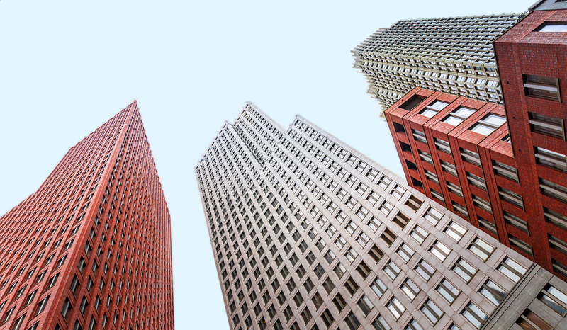 Upward view of three modern skyscrapers with varying designs and colors against a clear blue sky.