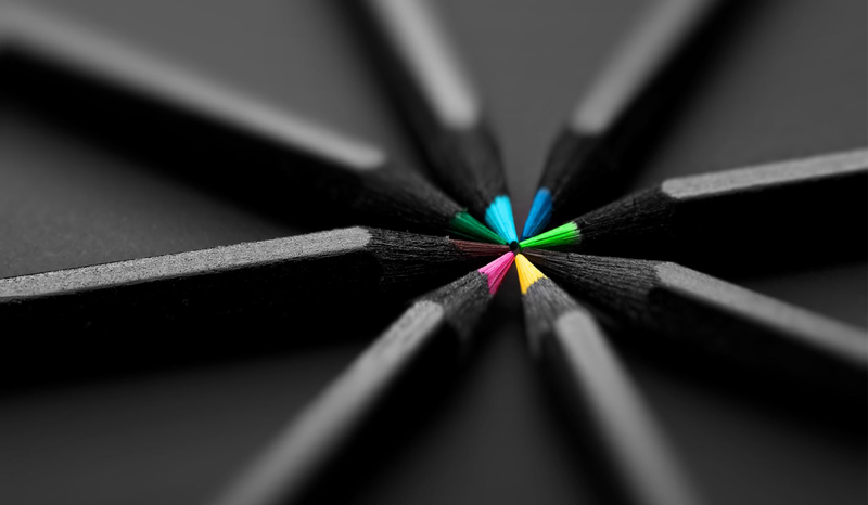Close-up of colored pencil tips arranged in a circular pattern on a dark background, showcasing vibrant colors like blue, green, and pink.
