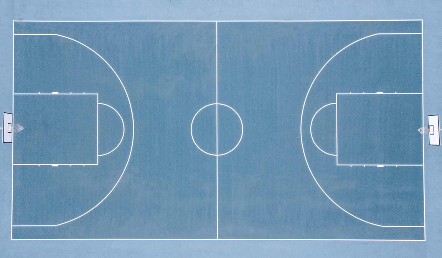 Aerial view of an empty blue basketball court with white lines, showing two hoops and a central circle.