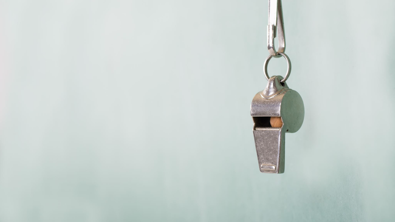 A silver whistle hanging against a light blue background.