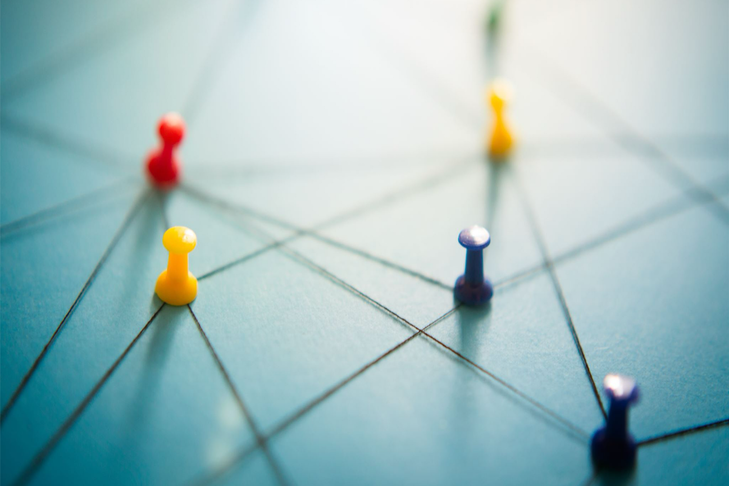 Colored pushpins connected by lines on a blue surface, representing a network or connections.
