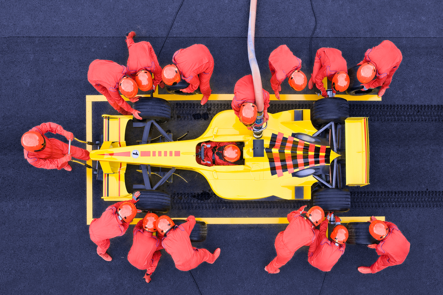 Aerial view of a yellow Formula 1 car in a pit stop, surrounded by a team in red uniforms performing maintenance.