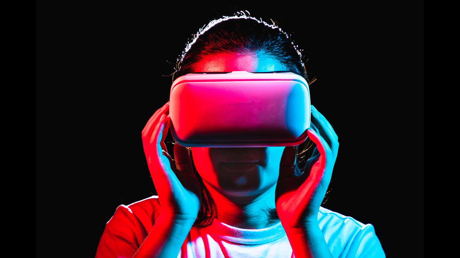 Person wearing a virtual reality headset, illuminated by red and blue lights against a dark background.