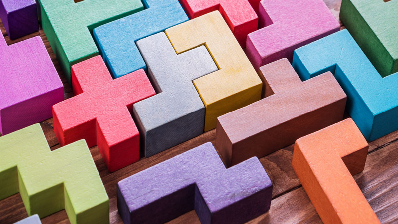 Colorful wooden Tetris-like blocks arranged on a wooden surface, forming an interlocking pattern.