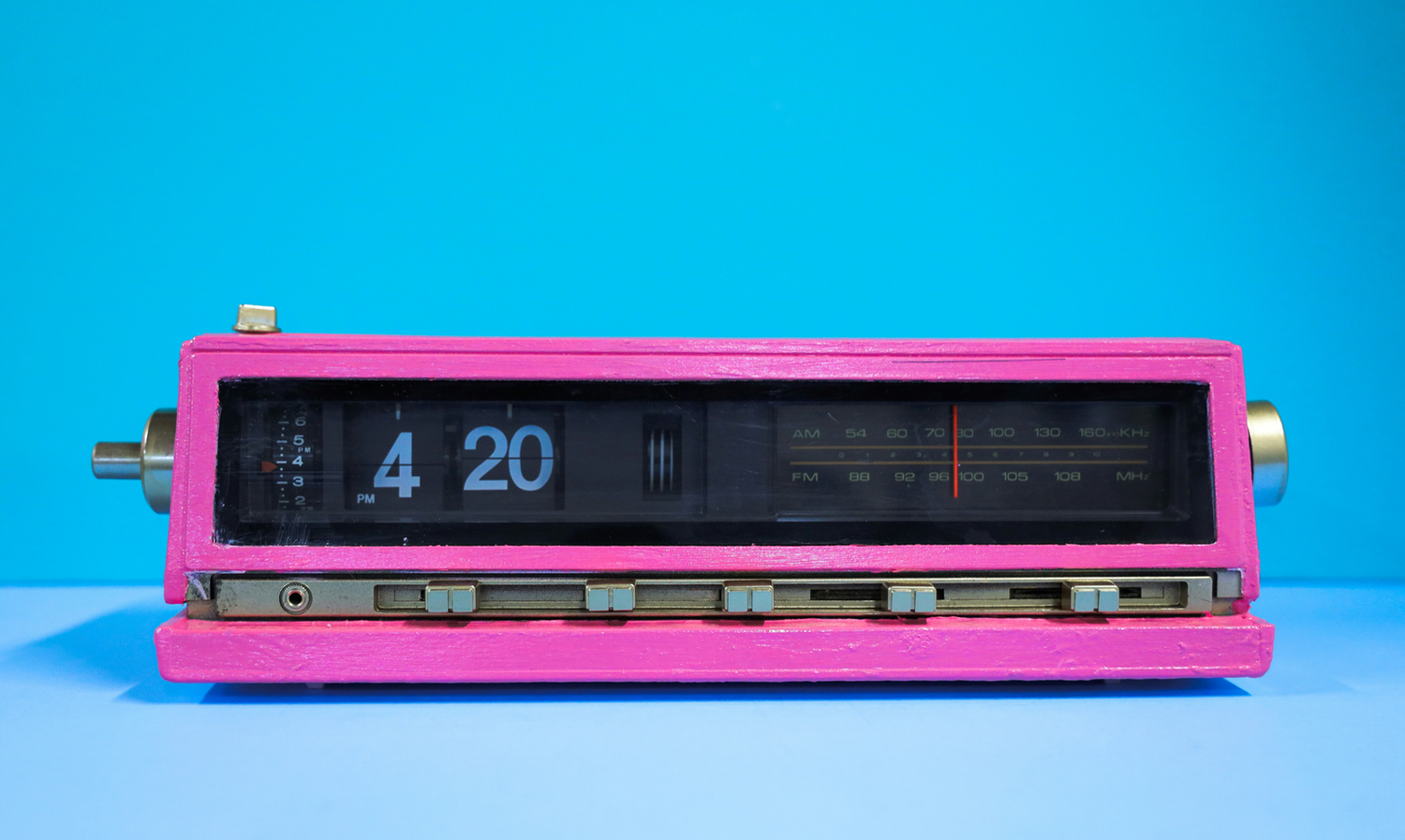 A vintage pink flip clock radio displaying 4:20, set against a bright blue background.