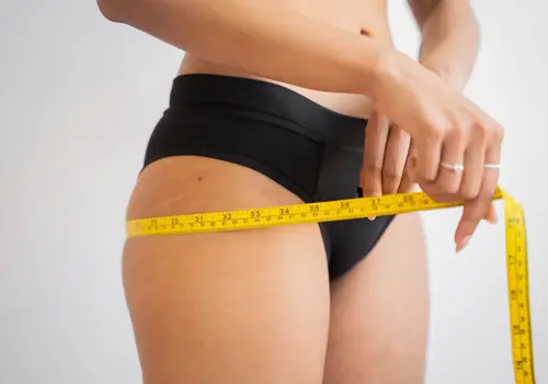 Woman measuring her hip circumference with a tape measure.