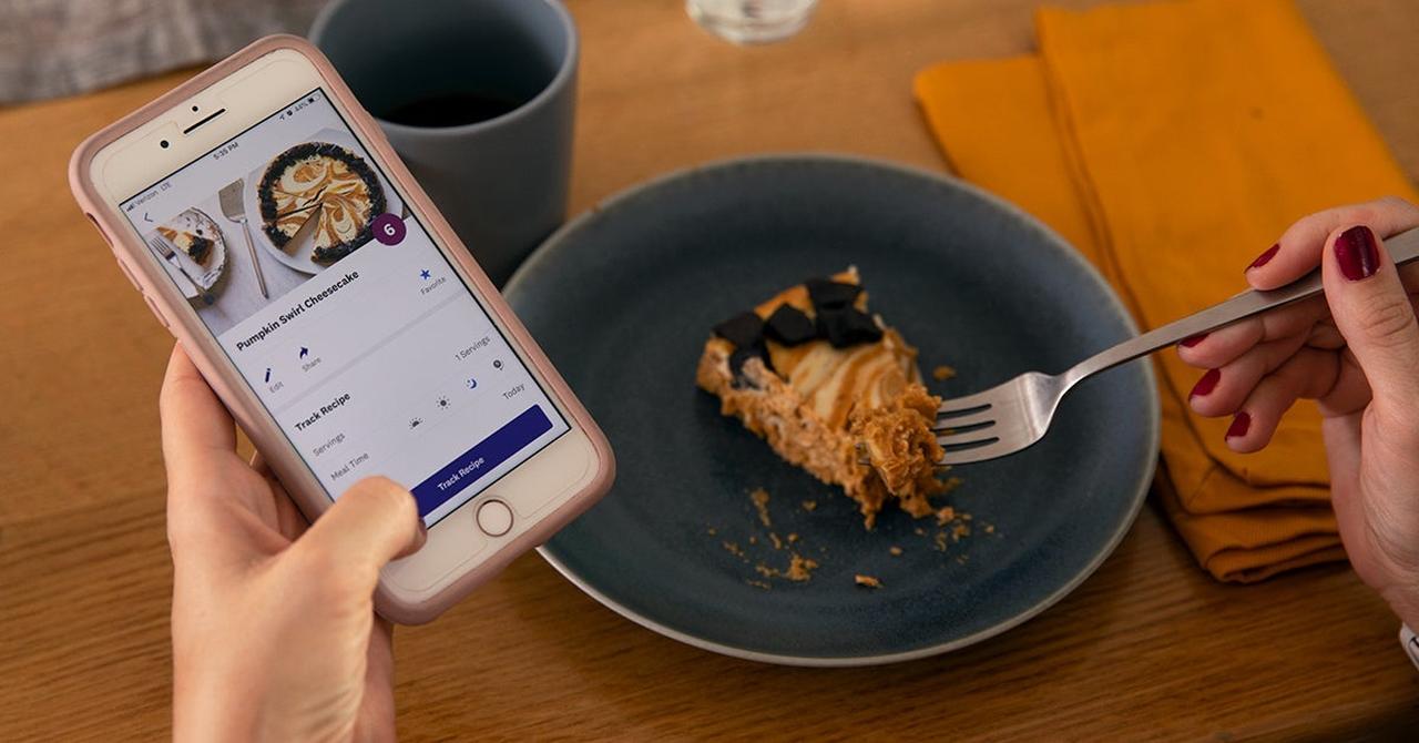 Woman tracks a slice of pumpkin cheesecake on her phone, with a fork taking a bite.
