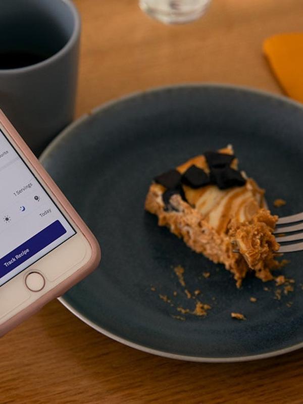 Woman tracks a slice of pumpkin cheesecake on her phone, with a fork taking a bite.