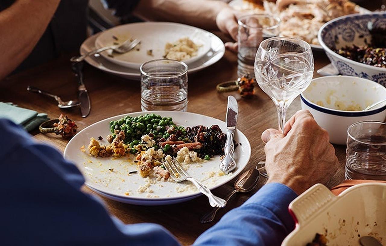 Partially eaten meal on a plate with peas and stuffing, and glasses of water on a wooden table.