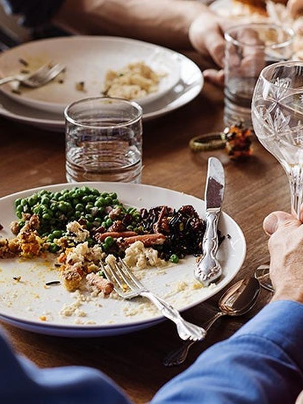 Partially eaten meal on a plate with peas and stuffing, and glasses of water on a wooden table.