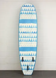 A surfboard with blue and white geometric patterns, featuring triangles and stripes, stands against a light brick wall.