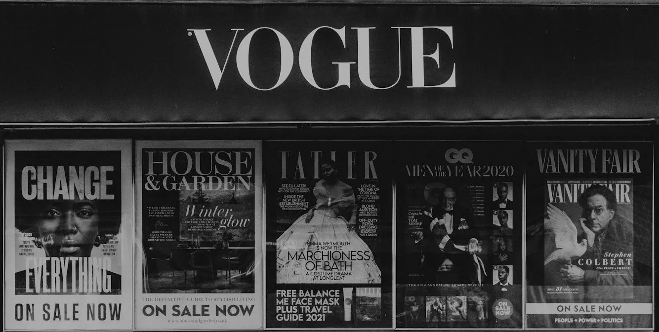 Magazine stand displaying covers of Vogue, House & Garden, Tatler, GQ, and Vanity Fair. Bold "VOGUE" sign above.