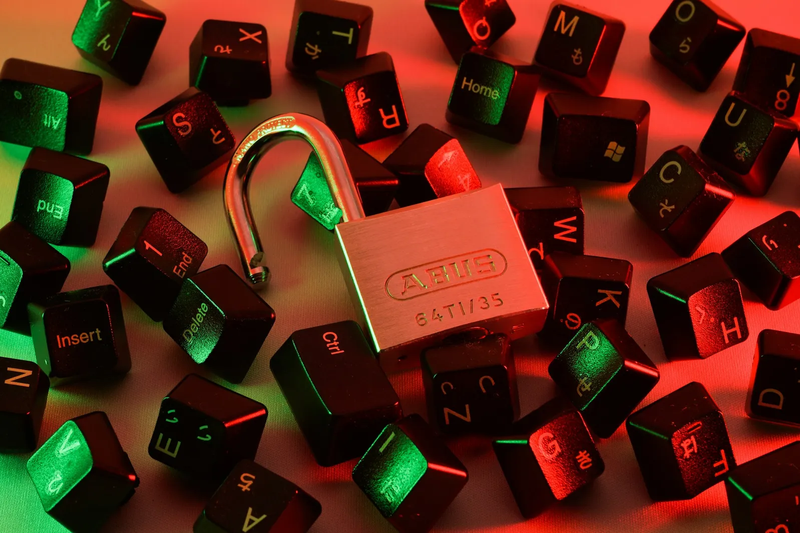 An open padlock surrounded by scattered keyboard keys under red and green lighting.