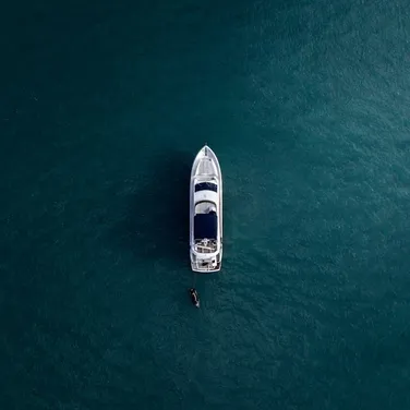 Aerial view of yacht floating on calm, deep blue water, with a small boat attached to its side.