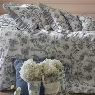 Floral-patterned bedding with ruffled pillows, accompanied by a bag of white flowers on a bed.