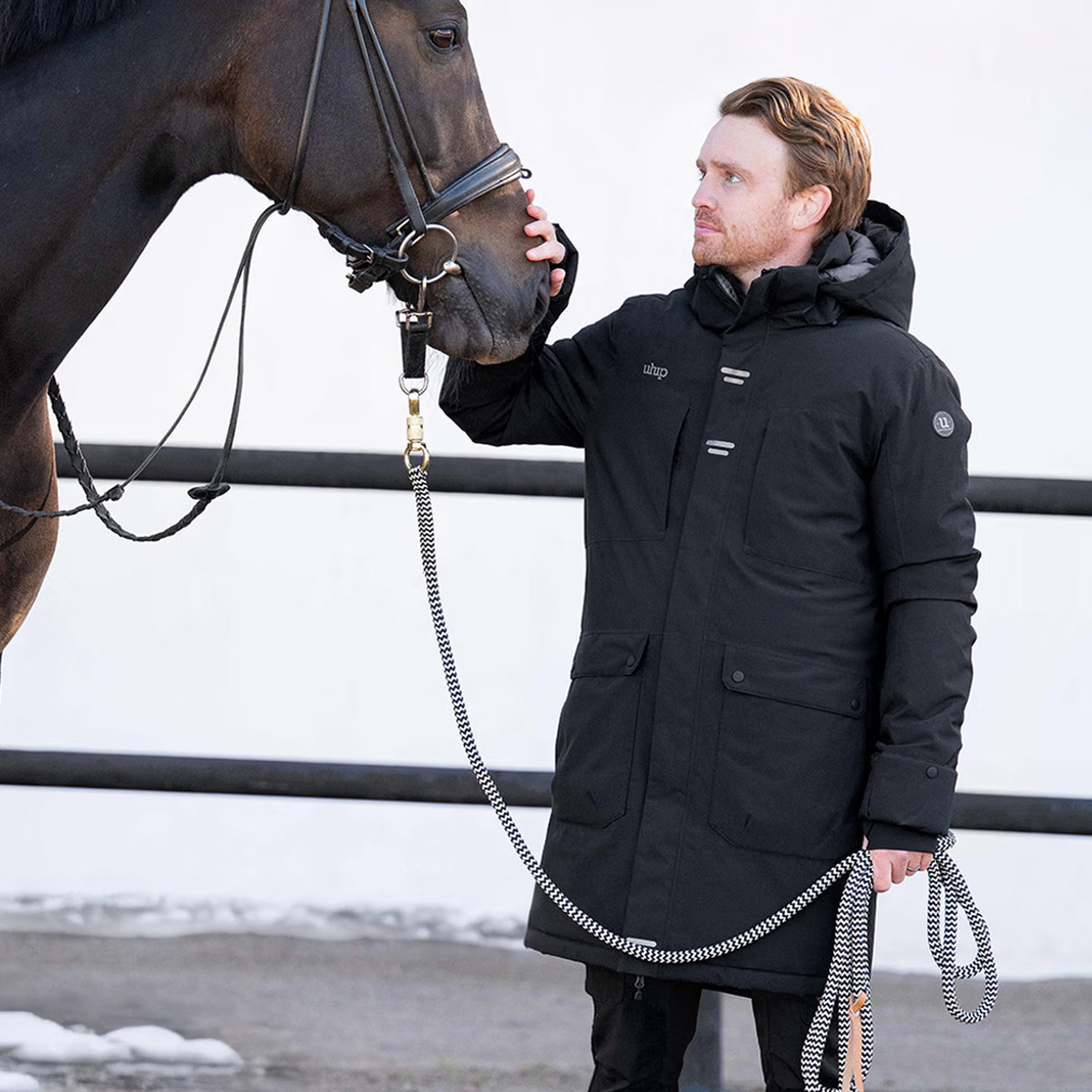 Man in a black Urban Strech Winter Riding Parka coat standing in front of a white background.