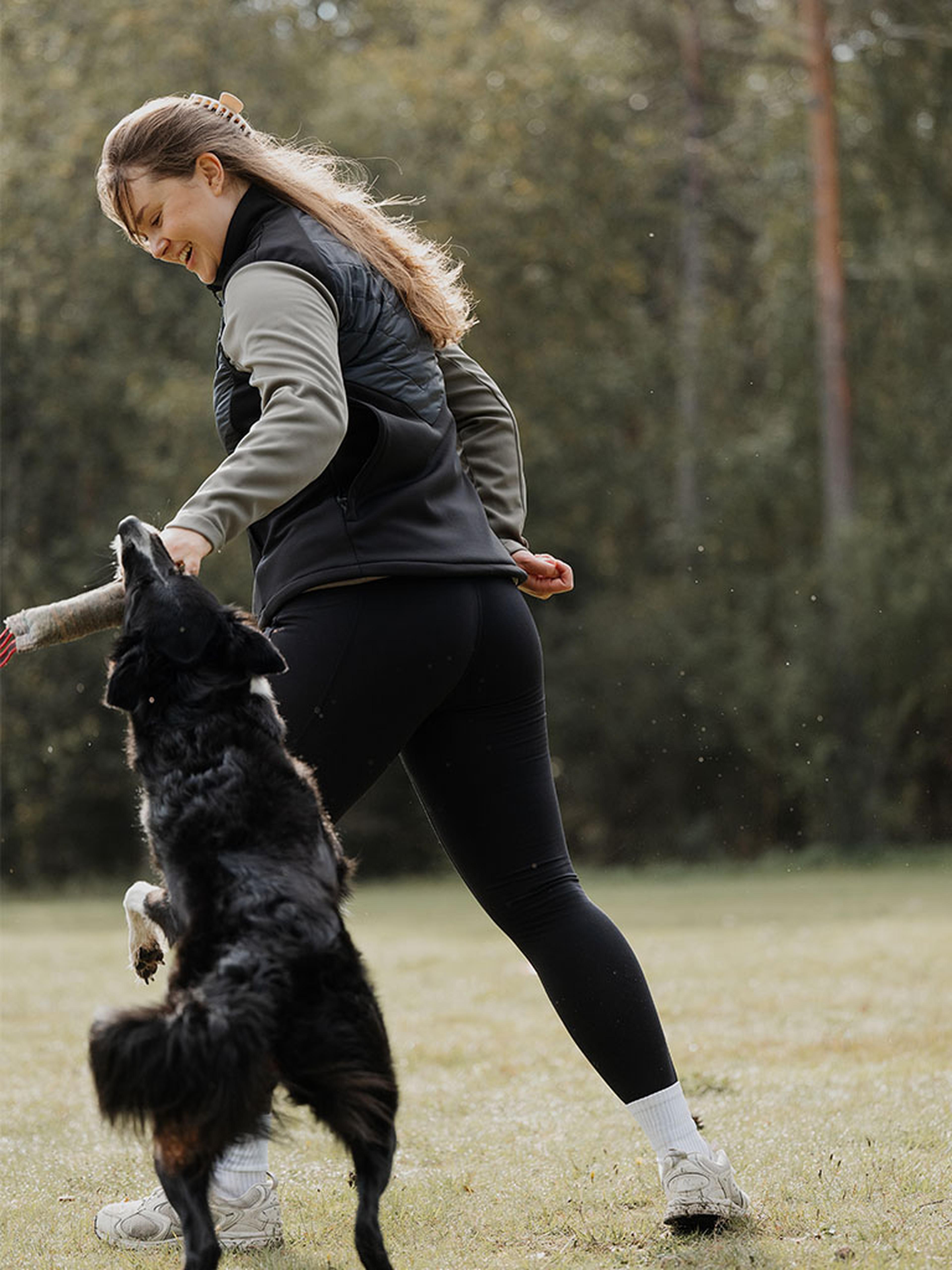 Woman playing with a dog in a black Misty Hybrid Vest.