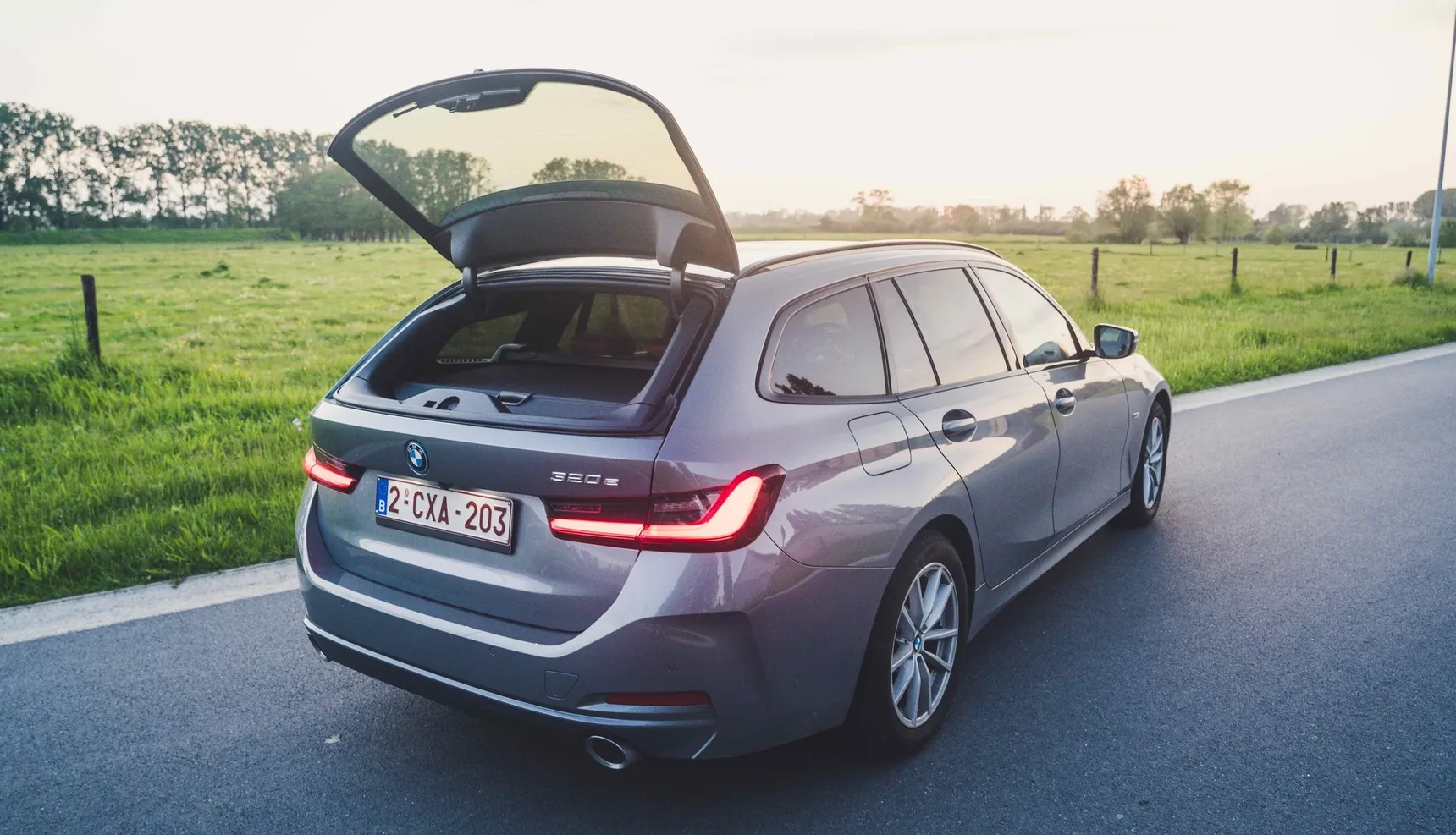 2024 BMW 320e Touring rear window open trunk sunset grass fields