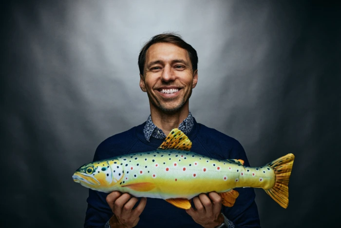 Johan Attby smiling while holding a fish plushy infront of him