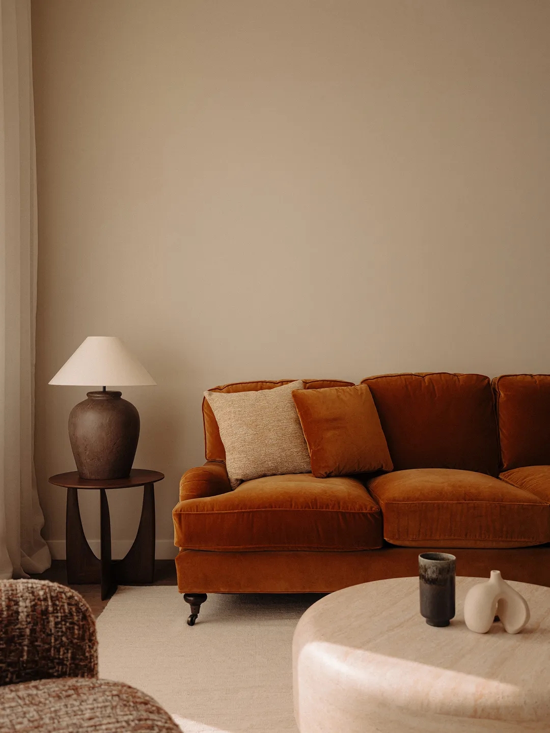 Cozy room with an orange sofa, side table with lamp, and a round coffee table decorated with a black cup and abstract sculpture.