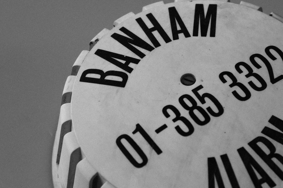 Black and white close-up of a vintage Banham alarm sign with numbers on a faceted surface against a plain background.