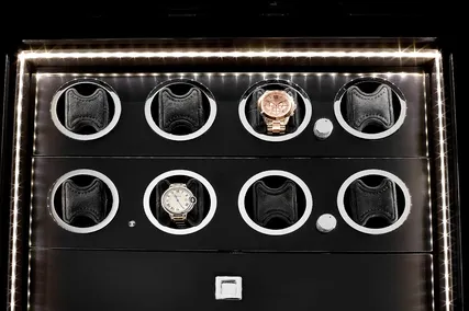 A luxury watch storage case with LED lighting, showcasing two watches among empty slots.