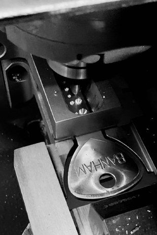 Close-up of a Banham key being cut on a precision key-cutting machine, with metal shavings and grooves visible.