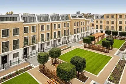 Modern townhouse complex with neatly landscaped garden, featuring green lawns, trimmed trees, and wooden pergolas on a clear day.