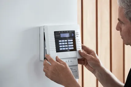 Man adjusting a wall-mounted electronic security panel with a keypad, in a modern setting.