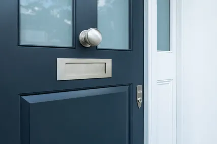 Close-up of a black door with a chrome doorknob, letterbox, and lock, next to a white door.