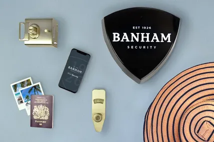 A Banham security system with a lock, smartphone, passport, photos, and a hat arranged on a blue surface.