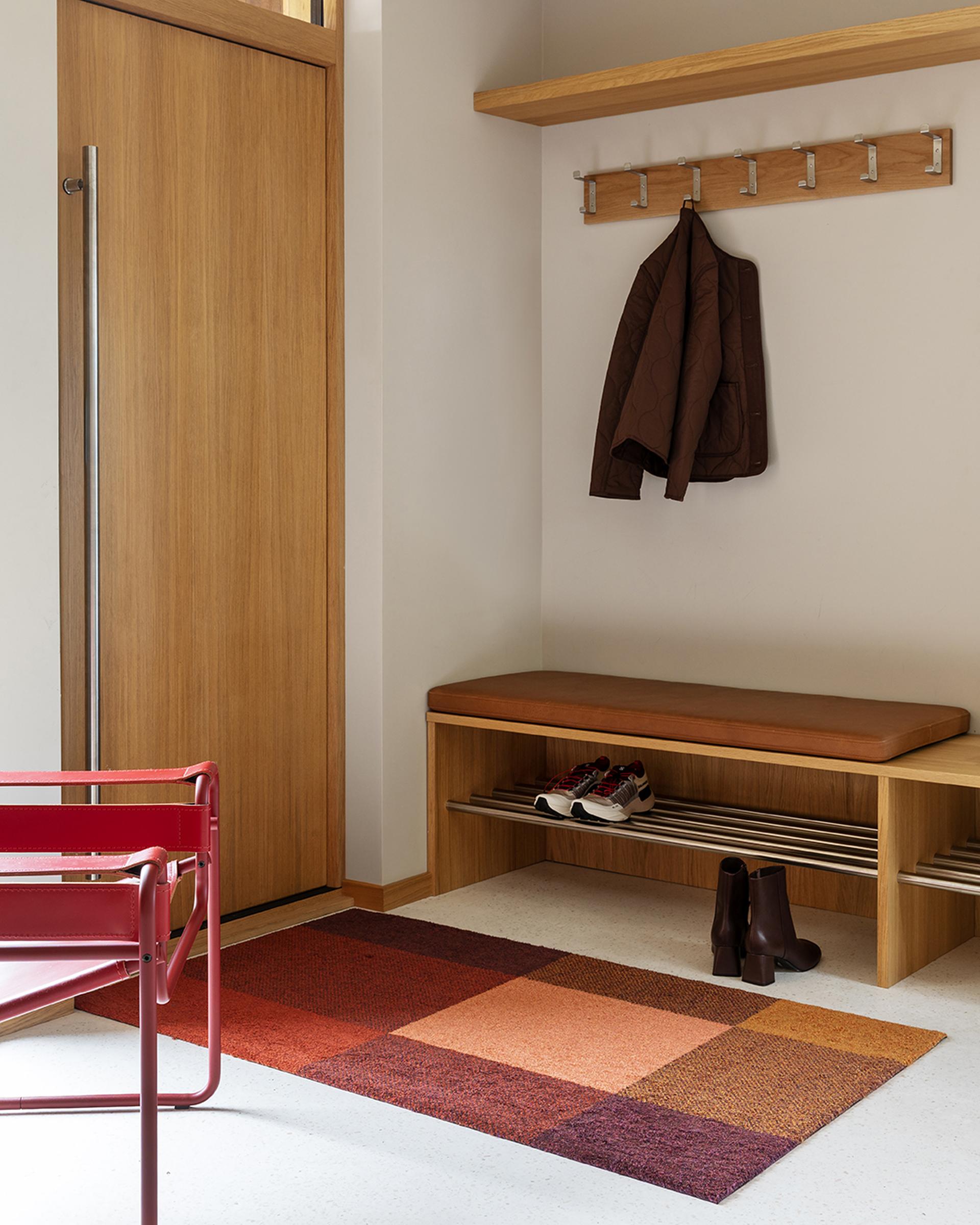Heymat Mix Ember doormat in a minimalist entryway with red chair and wood details