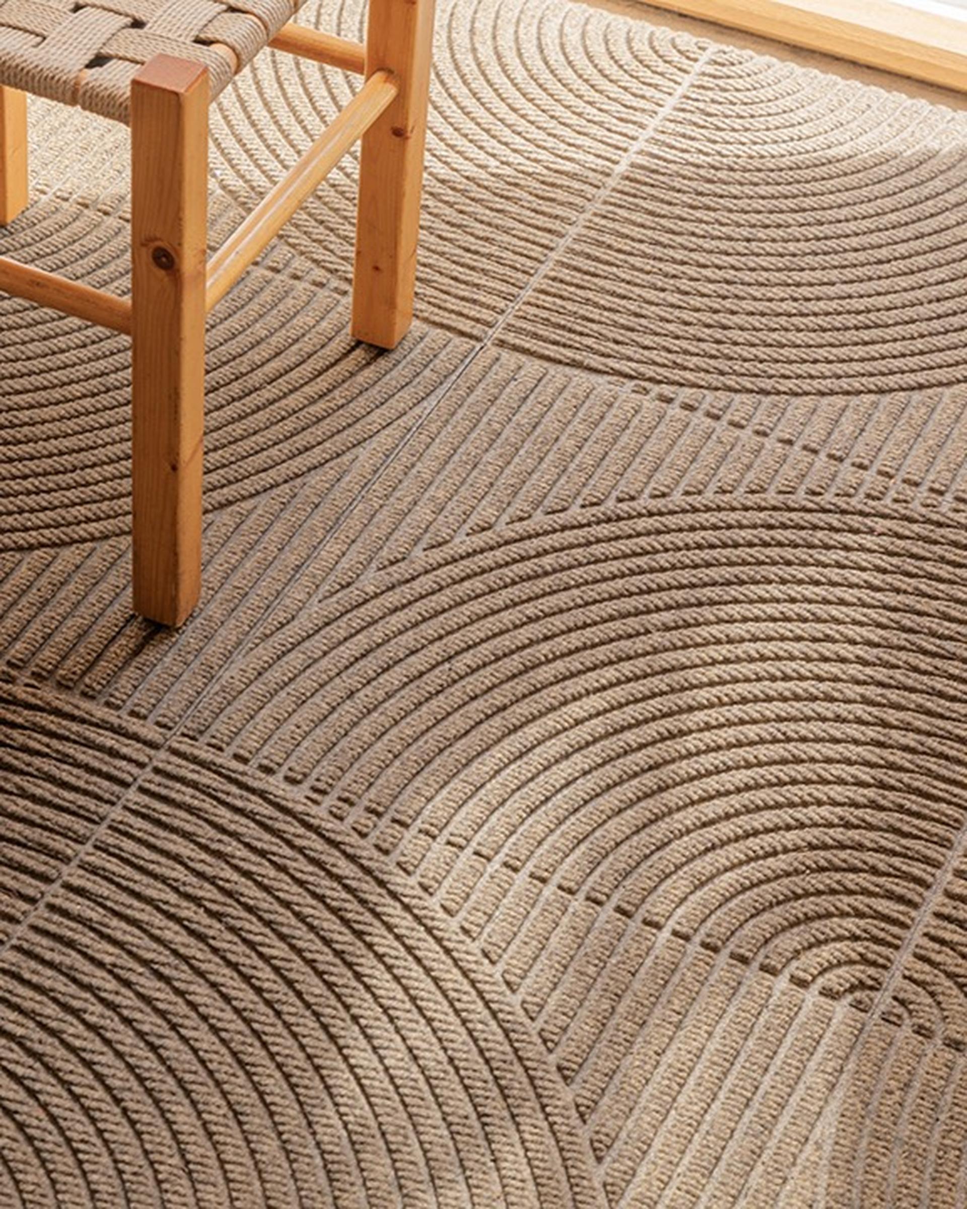 A wooden chair on a textured carpet tiles from Heymat with circular patterns in a sunlit room.