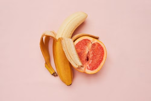 Eine Banane und eine Blut-Orange die nebeneinander liegen vor einem rosanen Hintergrund