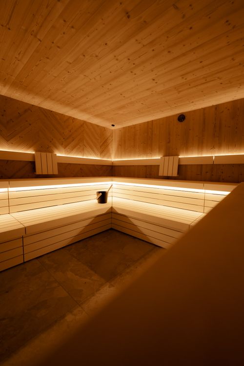 Holzverkleidete Sauna in der IKUNA Saunawelt mit Sitzbänken über Eck und warmer, indirekter Beleuchtung. Auf einer Bank stehen ein Aufgusseimer und eine Kelle.