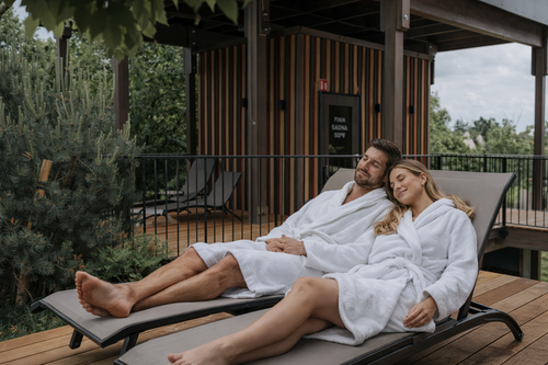 IKUNA_Wellness_PärchenZEIT Ein Pärchen liegt vor der Sauna gemütlich auf zwei Liegestühlen mitten im Grünen in der IKUNA Camping Lodge.
