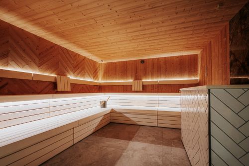 Sauna mit hellen Holzbänken, holzverkleideten Wänden und indirekter Beleuchtung in der IKUNA Spa- & Wellnesswelt in Natternbach, Oberösterreich. Auf einer Bank stehen ein Aufgusseimer und eine Kelle.