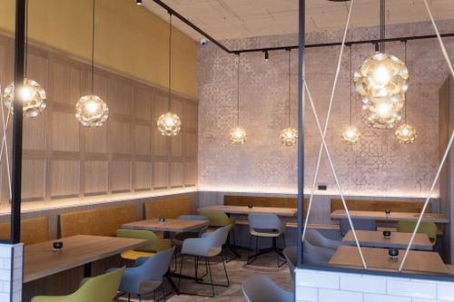 IKUNA Erlebnisbad Bistro Modernes Restaurantinterieur mit warmen Pendelleuchten, Holztischen, bunten Stühlen, gemusterten Wänden und einer gemütlichen, stilvollen Atmosphäre im IKUNA Erlebnisbad..