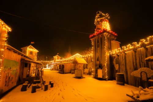 IKUNA Lichterwelt in WInterlandschaft Eine gemütlich, festlich geschmückte Piratenwelt bei Nacht, beleuchtet von warmen Lichterketten. Holzgebäude und schneebedeckter Boden schaffen eine ruhige, winterliche Atmosphäre.