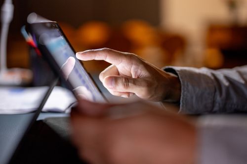 Nahaufnahme eines Tablets, welches eine Person in der Hand hält. Im Hintergrund ist ein verschwommenes Ambiente im IKUNA Naturresort.
