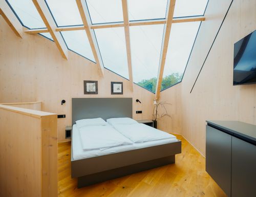 Sternenhimmelchalet Modernes Schlafzimmer im IKUNA Sternenhimmelchalet mit gemütlichem Doppelbett, heller Holzverkleidung und großzügigen Dachfenstern für den Blick in den Sternenhimmel.