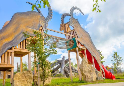 IKUNA Naturresort Dřevěné hřiště s sochami dvou velkých horských koz, jejichž rohy se proplétají. Součástí konstrukce je lanový most, skluzavka a přírodní prvky, které v resortu IKUNA Naturresort navozují hravou a dobrodružnou atmosféru.
