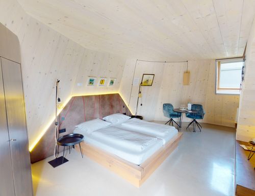 Modernes Schlafzimmer mit Holzwänden, Doppelbett, seitlichem Tisch mit zwei Stühlen, dekorativen Bildern und Fenster. Minimalistisches Design.