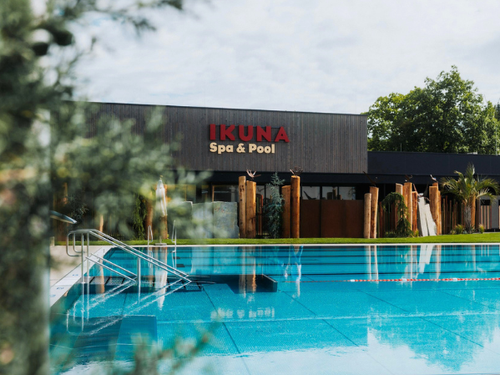 IKUNA Erlebnisbad Erlebnisbadbecken vor dem modernen Spa-Gebäude namens IKUNA Spa & Pool, umgeben von Bäumen und großzügigen Grünflächen in Natternbach.