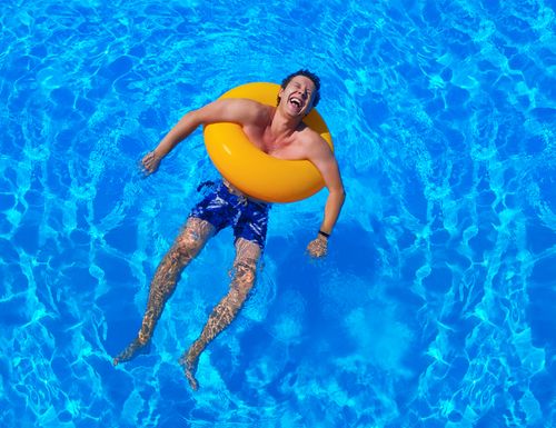 IKUNA_Erlebnisbad_Mann_Schwimmreifen Mann chillt im Wasser mit orangefarbenen Schwimmreifen