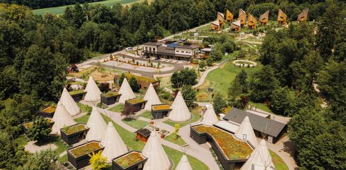 Luftaufnahme des IKUNA Naturresort mit zahlreichen weißen Tipis in einer ruhigen, idyllischen Umgebung, die sich durch ihre grünen Wiesen, gewundenen Wege und Holzhütten auszeichnet.