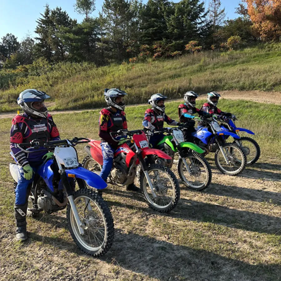 Group of dirt bike riders lined up on an open dirt track.
