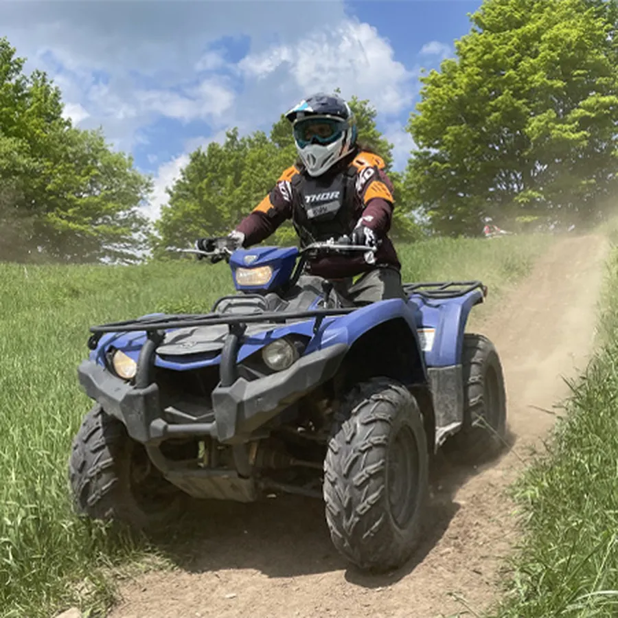Person riding a blue ATV on a dirt trail surrounded by green trees.