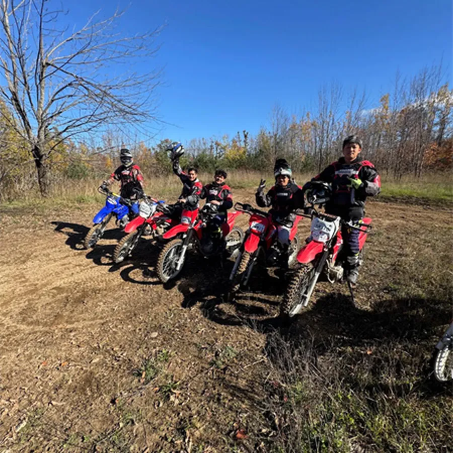 Group of dirt bike riders posing together on a dirt trail.